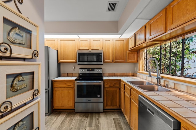 kitchen with a sink, appliances with stainless steel finishes, and tile countertops