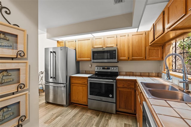 kitchen with visible vents, a sink, light wood-style floors, tile counters, and stainless steel appliances