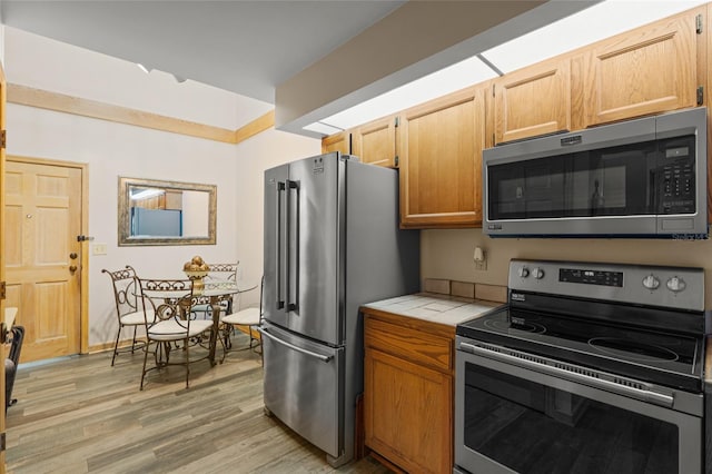 kitchen featuring tile countertops, light wood-style flooring, and appliances with stainless steel finishes