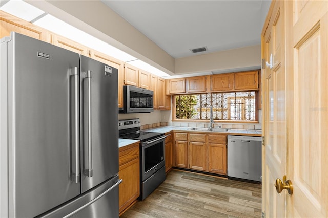 kitchen with tile countertops, visible vents, a sink, light wood finished floors, and stainless steel appliances
