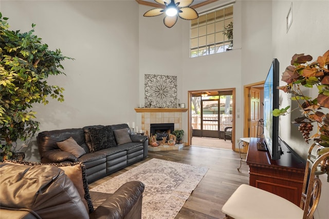 living room featuring a ceiling fan, a high ceiling, wood finished floors, and a tile fireplace