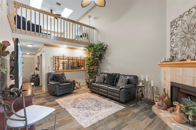 living area with visible vents, a skylight, a towering ceiling, a tile fireplace, and wood finished floors