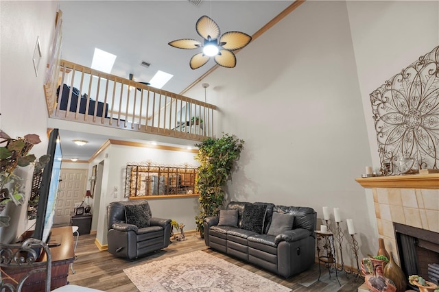 living area with visible vents, wood finished floors, high vaulted ceiling, a tile fireplace, and a skylight