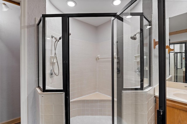 full bathroom featuring vanity, a textured wall, and a stall shower