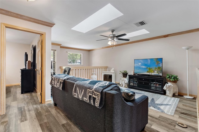 living room with ceiling fan, wood finished floors, a skylight, visible vents, and ornamental molding