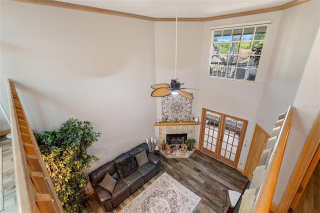 living area featuring crown molding, a fireplace, a ceiling fan, wood finished floors, and a towering ceiling