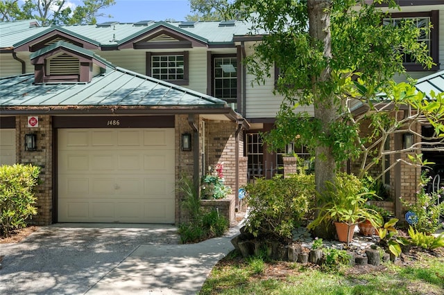 townhome / multi-family property featuring an attached garage, driveway, brick siding, and metal roof