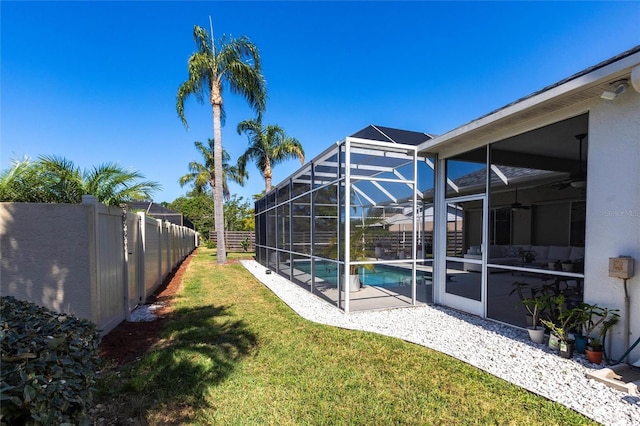 view of yard with ceiling fan, glass enclosure, fence, a fenced in pool, and a patio