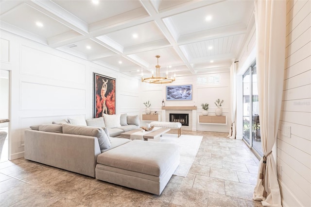 living area with stone finish floor, beamed ceiling, a decorative wall, and a notable chandelier
