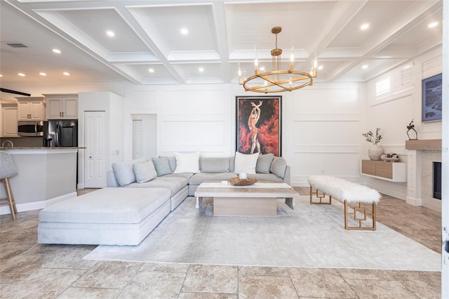 living room featuring a chandelier, beam ceiling, visible vents, and a decorative wall