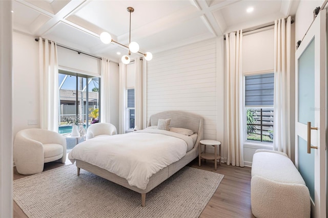 bedroom with access to outside, coffered ceiling, wood finished floors, and beam ceiling