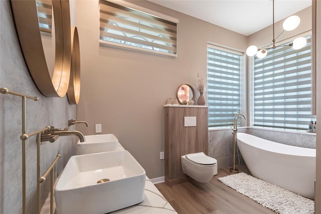 bathroom featuring a healthy amount of sunlight, dual sinks, wood finished floors, and a freestanding bath