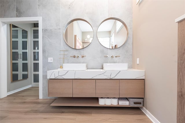 full bath with a sink, double vanity, and wood finished floors