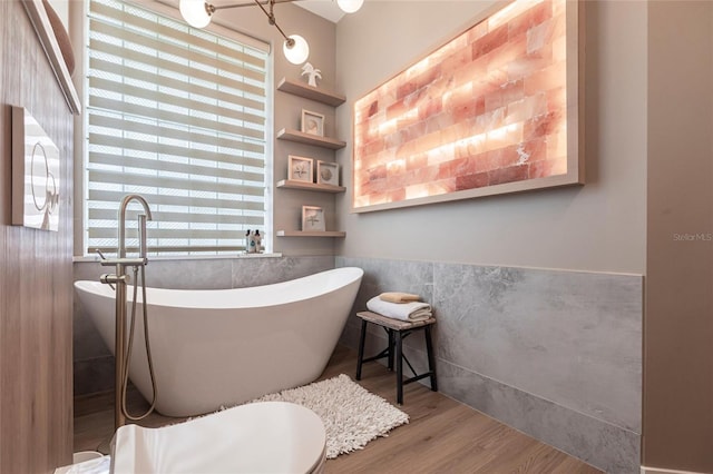 bathroom with a freestanding tub, tile walls, plenty of natural light, and wood finished floors