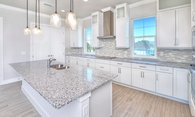 kitchen featuring wall chimney range hood, wood finish floors, a sink, black electric cooktop, and visible vents