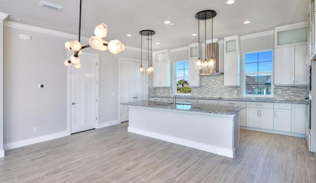 kitchen with crown molding, decorative backsplash, visible vents, and wall chimney range hood