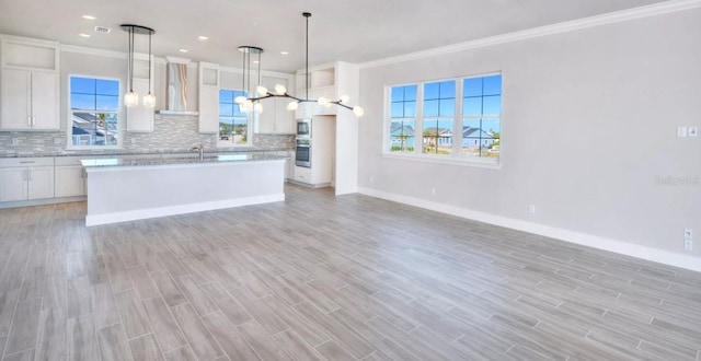 kitchen with wall chimney range hood, appliances with stainless steel finishes, a chandelier, ornamental molding, and open floor plan