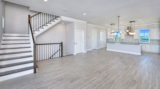 unfurnished living room featuring an inviting chandelier, recessed lighting, light wood-style floors, and crown molding