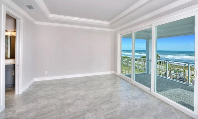 empty room with a water view, visible vents, crown molding, a raised ceiling, and a beach view