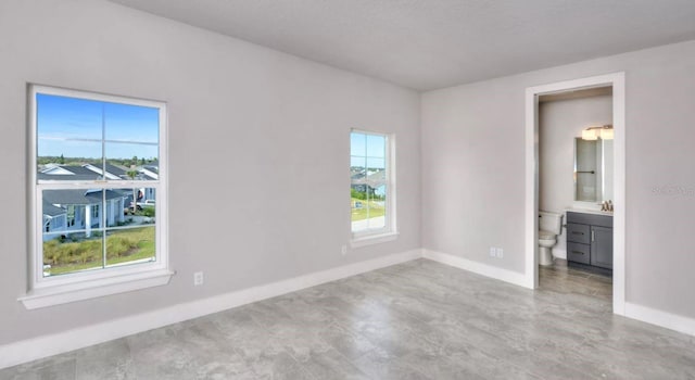 unfurnished bedroom with a sink, baseboards, multiple windows, and connected bathroom