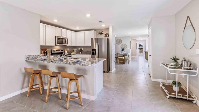 kitchen featuring a kitchen breakfast bar, appliances with stainless steel finishes, white cabinets, a peninsula, and light tile patterned flooring