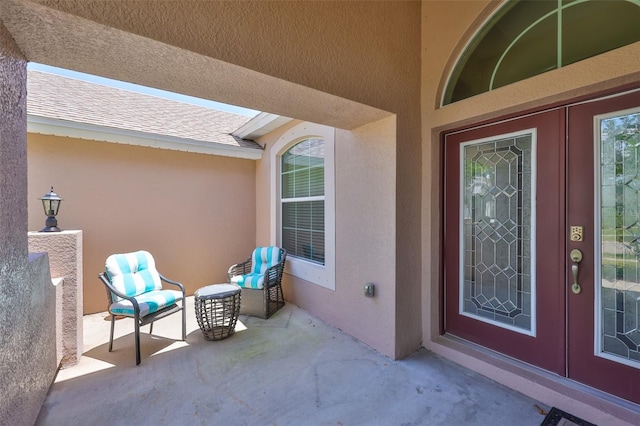 view of exterior entry with a patio area, stucco siding, and roof with shingles