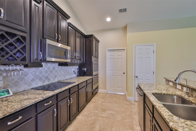 kitchen with dark brown cabinetry, tasteful backsplash, light stone countertops, a sink, and stainless steel appliances