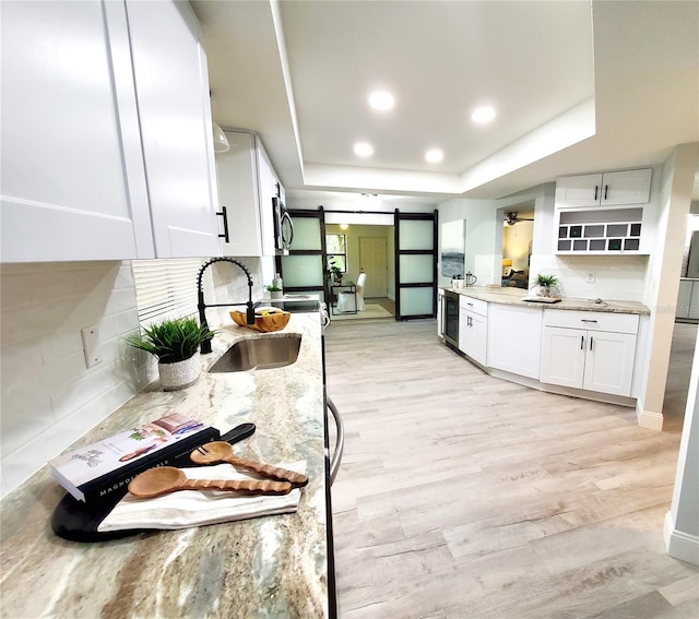 3529 Tanglewood Trl, Palm Harbor, FL 34685 - kitchen featuring light stone counters, a barn door, a sink, a raised ceiling, and white cabinetry