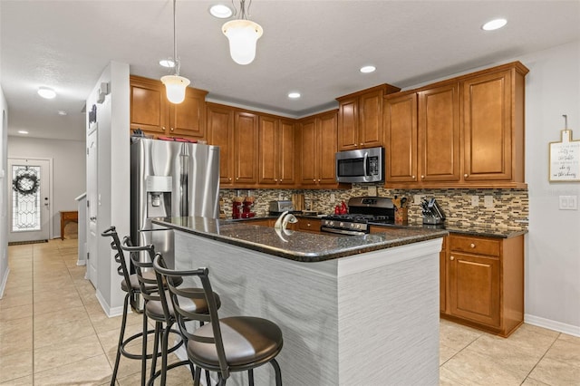 kitchen featuring backsplash, brown cabinets, light tile patterned floors, stainless steel appliances, and an island with sink