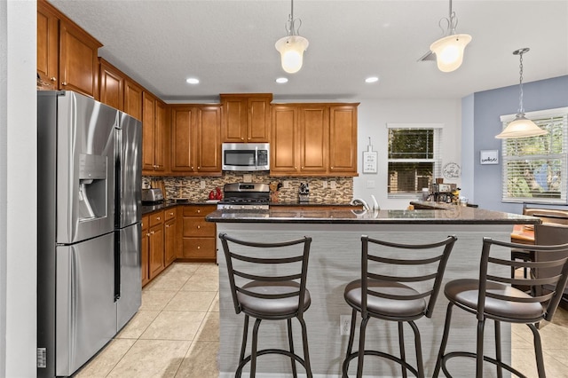 kitchen featuring brown cabinetry, appliances with stainless steel finishes, decorative backsplash, and light tile patterned floors