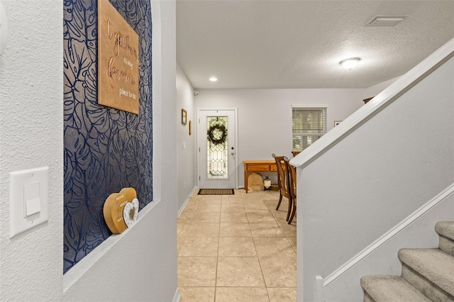 foyer with light tile patterned flooring, a textured ceiling, stairs, baseboards, and visible vents