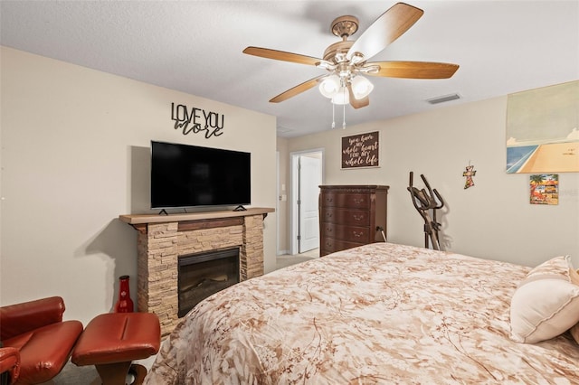 bedroom with visible vents, ceiling fan, and a stone fireplace