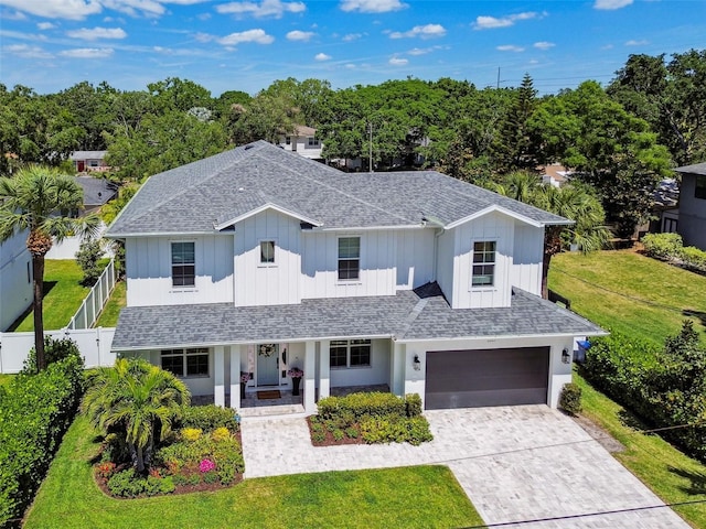 traditional home featuring board and batten siding, roof with shingles, decorative driveway, and covered porch