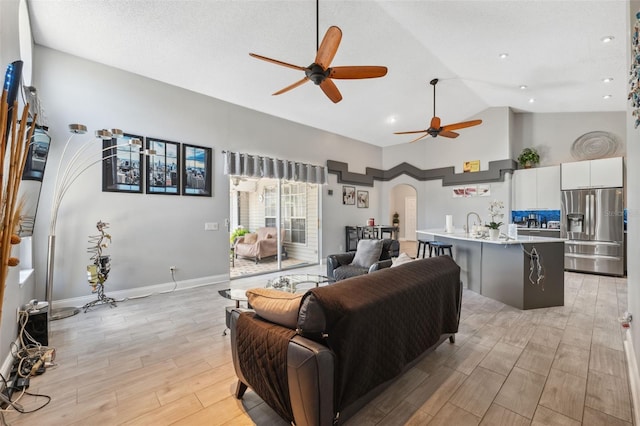living room featuring a ceiling fan, arched walkways, high vaulted ceiling, recessed lighting, and light wood-style flooring
