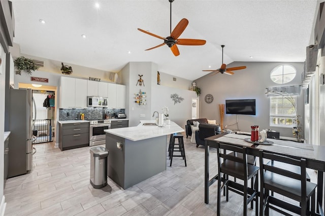 kitchen with a ceiling fan, an island with sink, white cabinetry, a sink, and stainless steel appliances