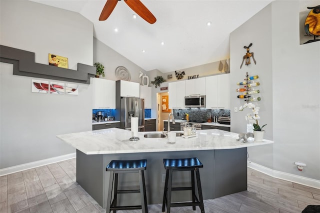 kitchen with a breakfast bar area, high vaulted ceiling, white cabinets, a sink, and stainless steel appliances