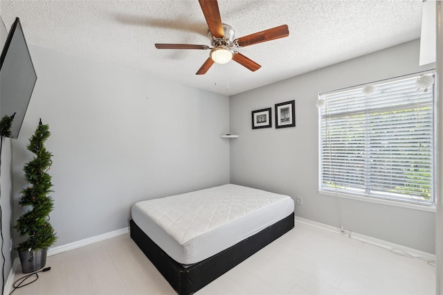 bedroom featuring a ceiling fan, a textured ceiling, and baseboards