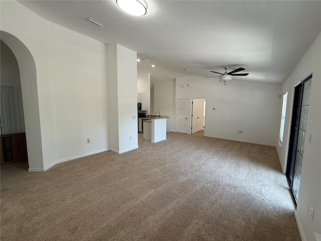 unfurnished living room with a ceiling fan, visible vents, light colored carpet, arched walkways, and lofted ceiling