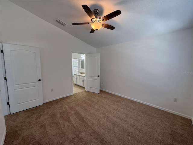 unfurnished bedroom with visible vents, light carpet, baseboards, ensuite bathroom, and vaulted ceiling