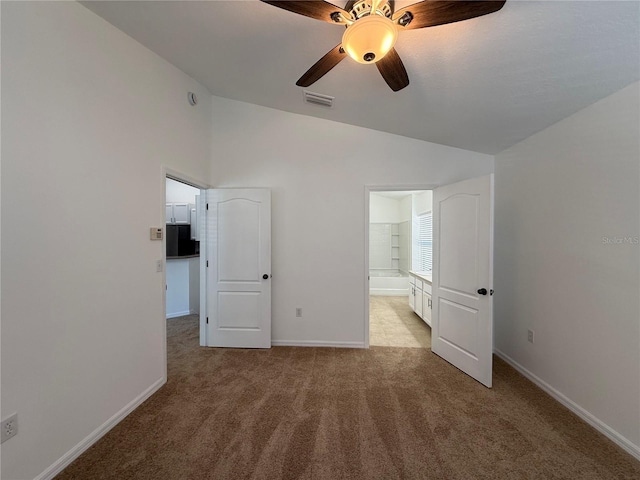 unfurnished bedroom featuring light colored carpet, visible vents, baseboards, ensuite bathroom, and vaulted ceiling