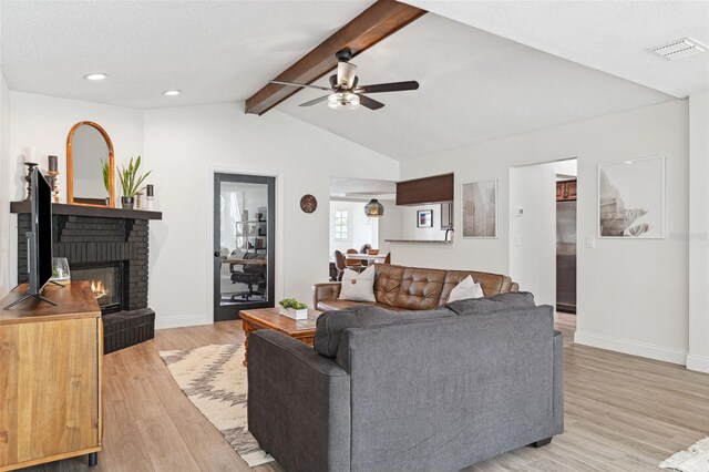 living room featuring a brick fireplace, light wood-style floors, baseboards, ceiling fan, and vaulted ceiling with beams