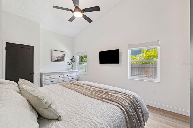 bedroom featuring light wood-type flooring, baseboards, ceiling fan, and high vaulted ceiling