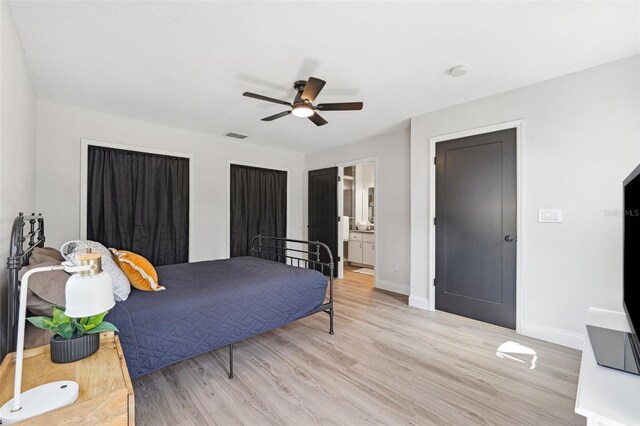bedroom featuring light wood-style floors, baseboards, ceiling fan, and ensuite bath