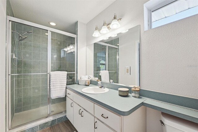 full bath with vanity, a textured wall, a stall shower, and wood finished floors