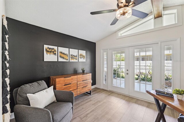 sitting room with an accent wall, lofted ceiling, wood finished floors, french doors, and a ceiling fan