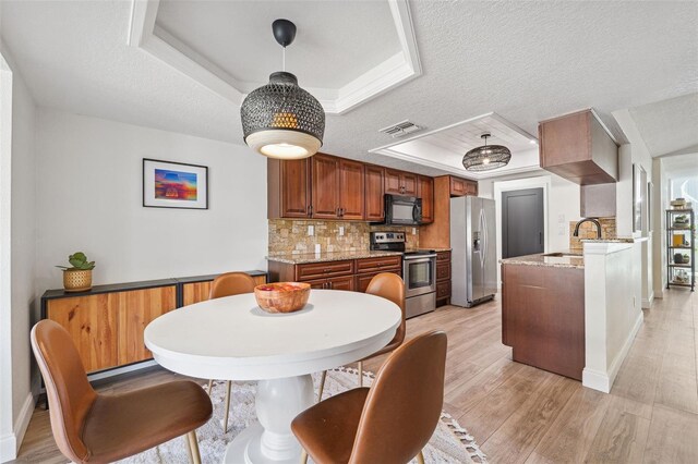 dining area with a textured ceiling, visible vents, baseboards, a tray ceiling, and light wood-style flooring