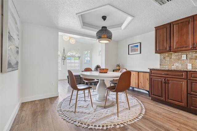 dining area featuring a textured ceiling, visible vents, baseboards, and light wood-type flooring