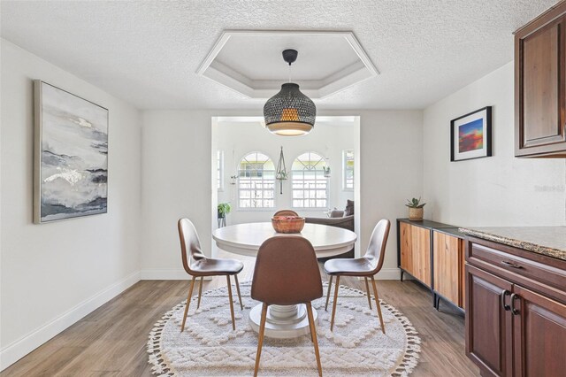 dining space featuring a textured ceiling, baseboards, a tray ceiling, and wood finished floors