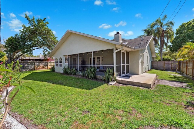 back of property with a sunroom, a lawn, stucco siding, and a chimney