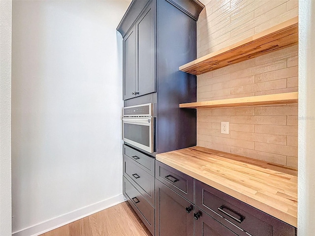 kitchen featuring oven, open shelves, wood counters, baseboards, and backsplash